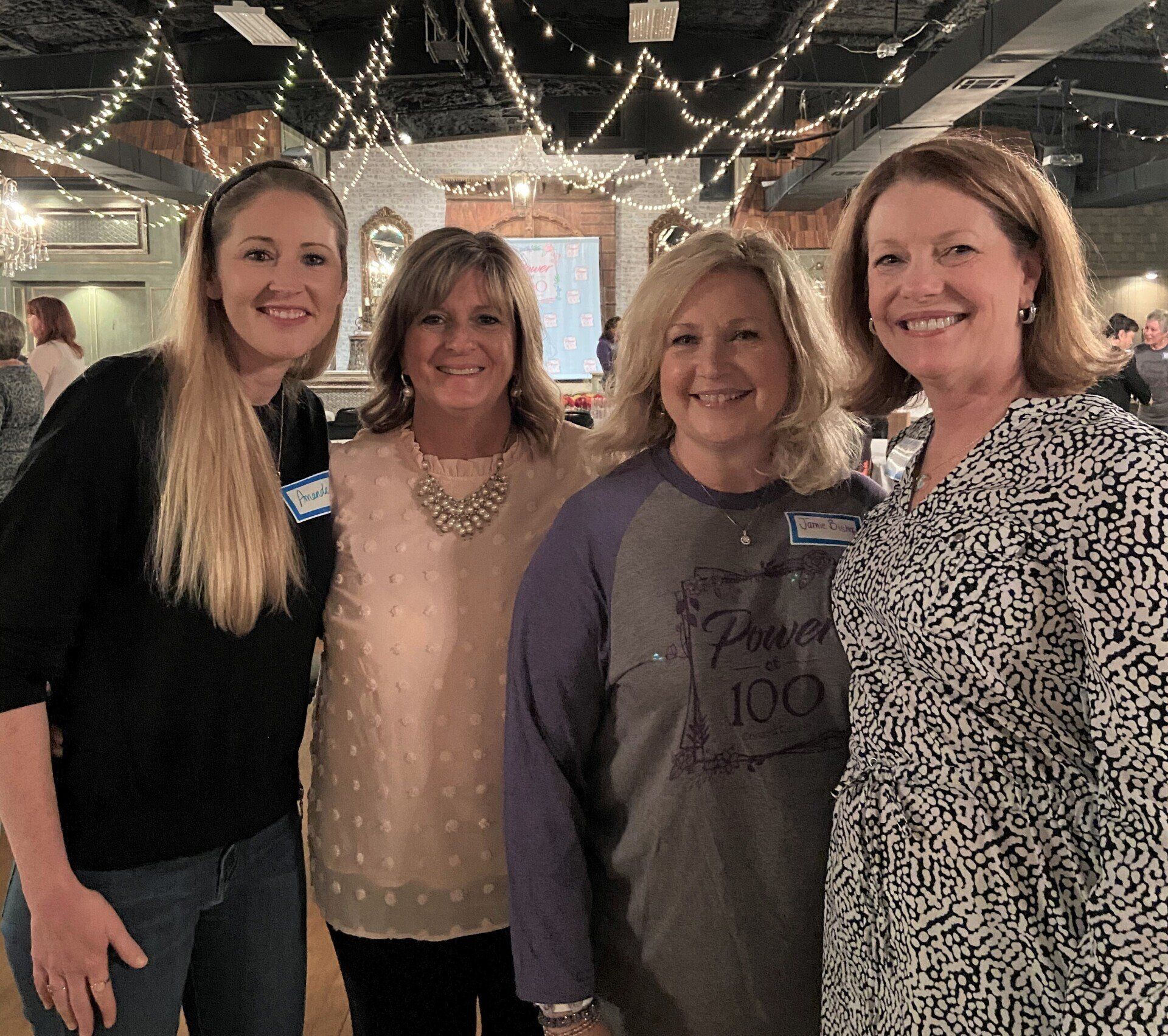 Four women posing for a picture with one wearing a shirt that says 100