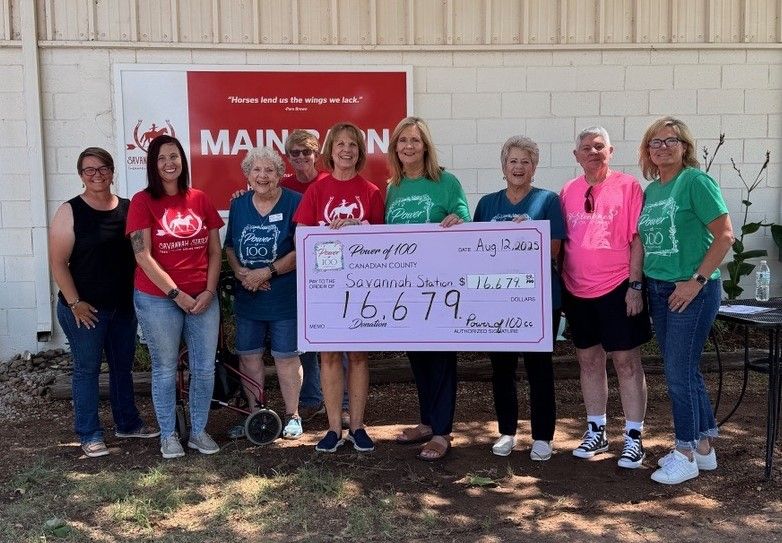 A group of people standing next to each other holding a large pink check.