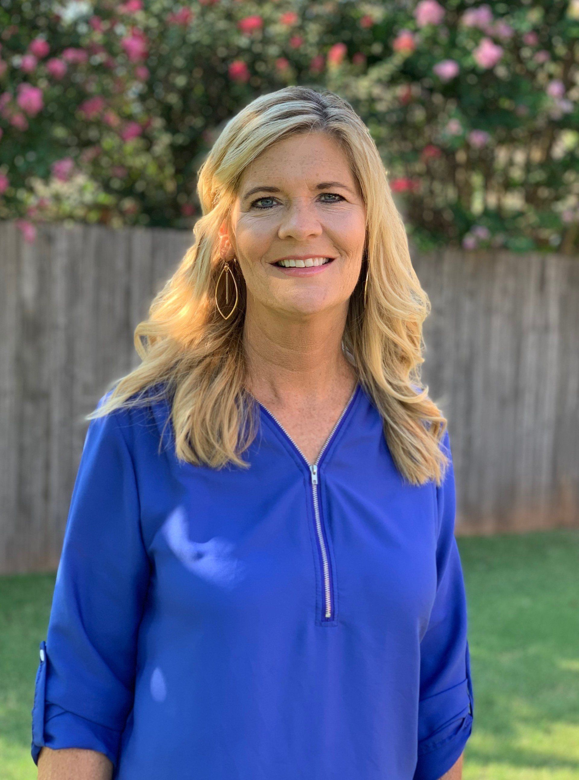 A woman in a blue shirt is standing in front of a fence.