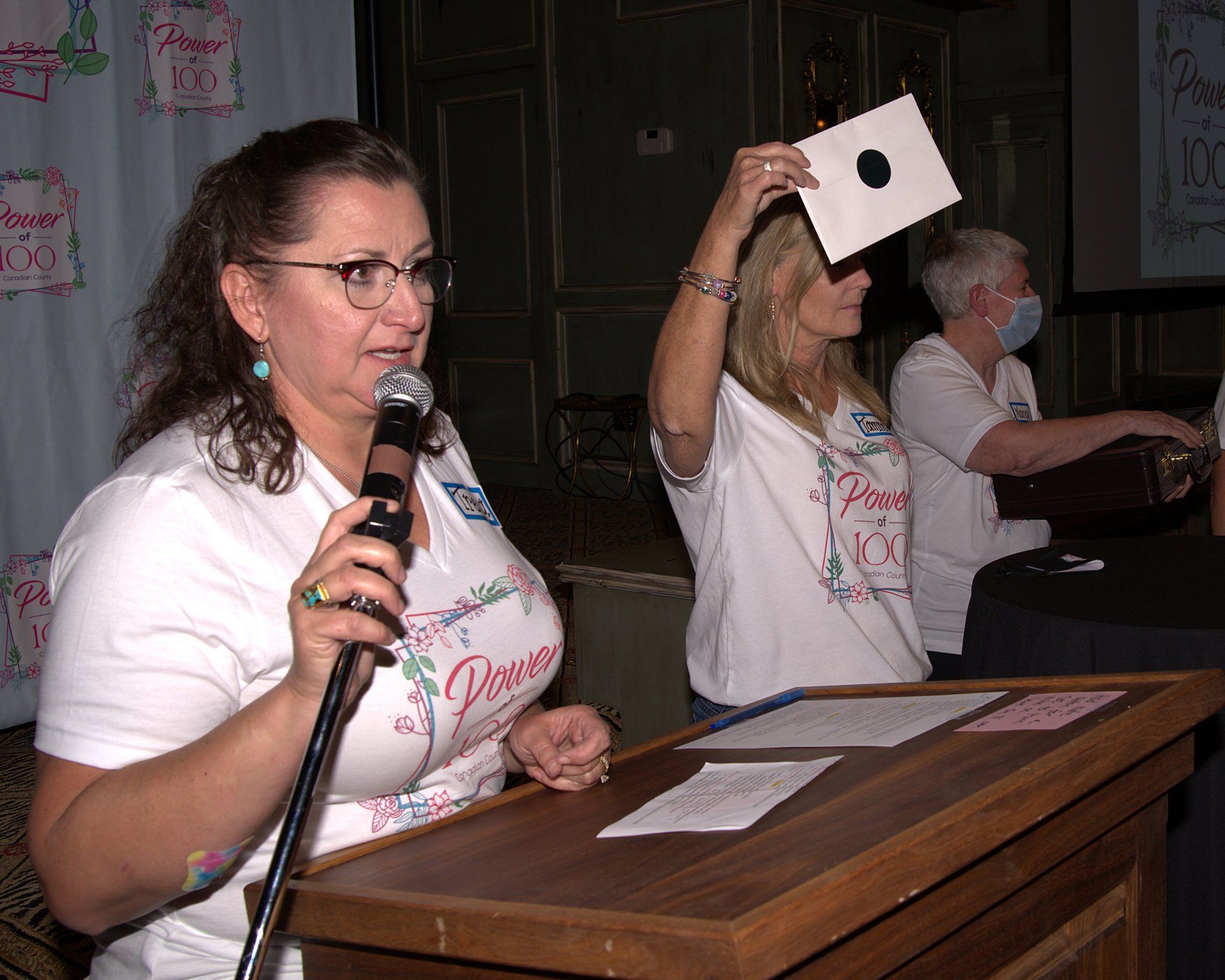 A woman is standing at a podium holding a piece of paper with a hole in it.