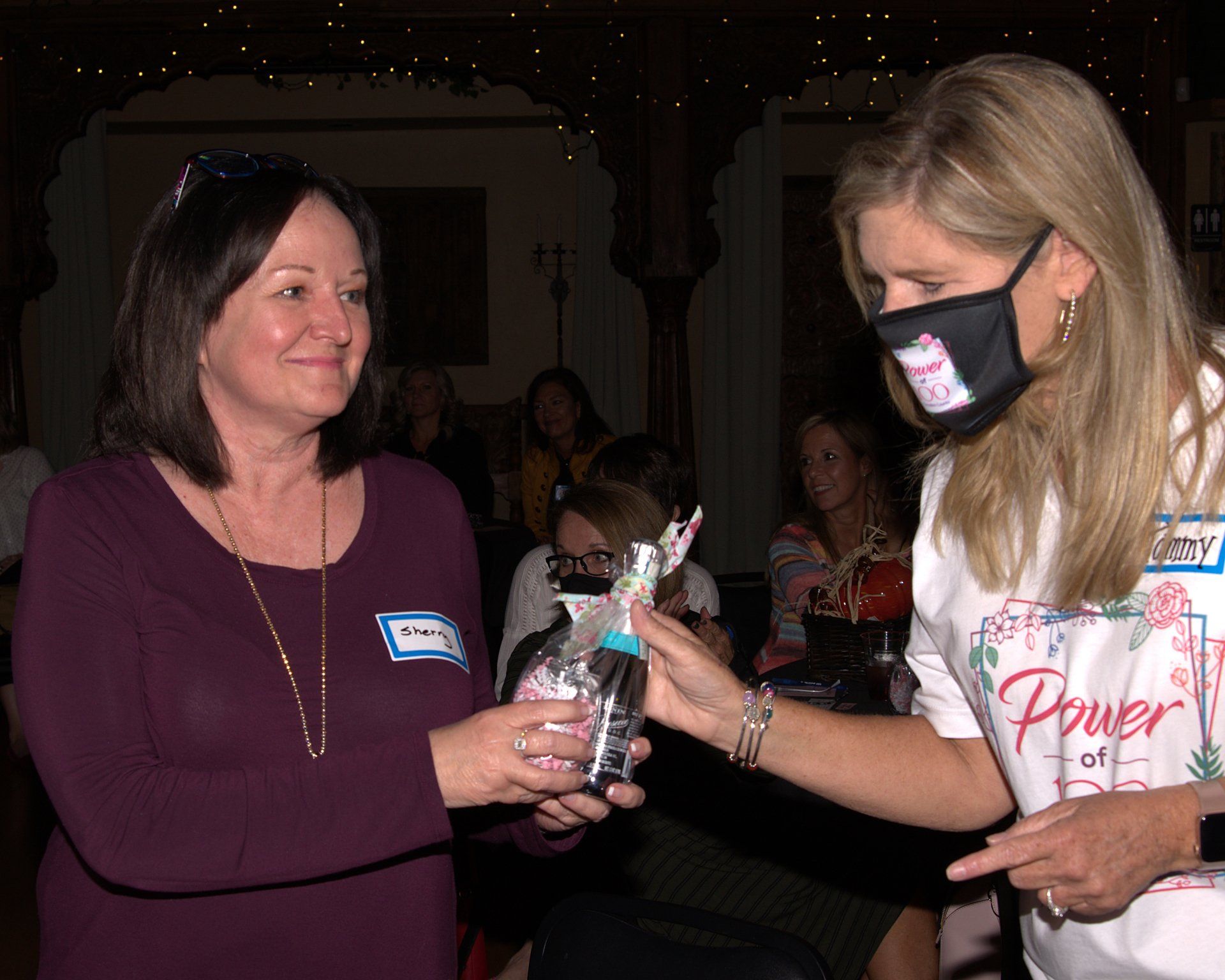 A woman wearing a mask is giving a gift to another woman.