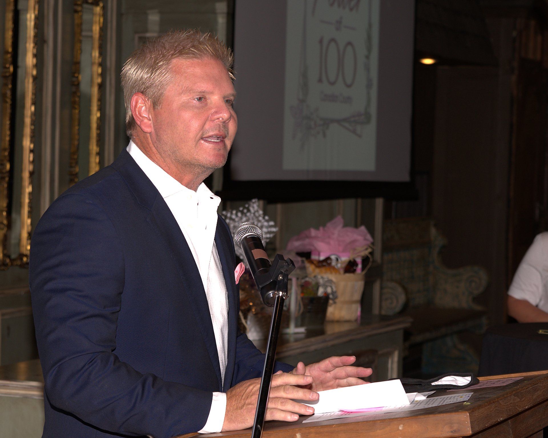 A man in a suit stands at a podium speaking into a microphone
