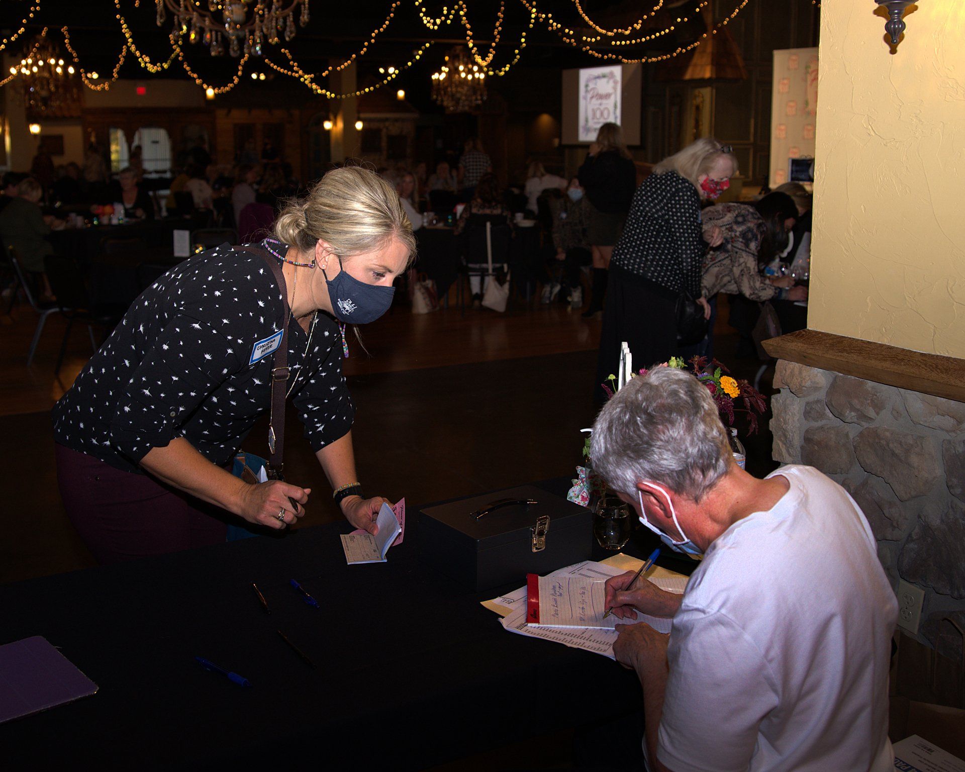 A woman wearing a mask is helping a man sign a form.