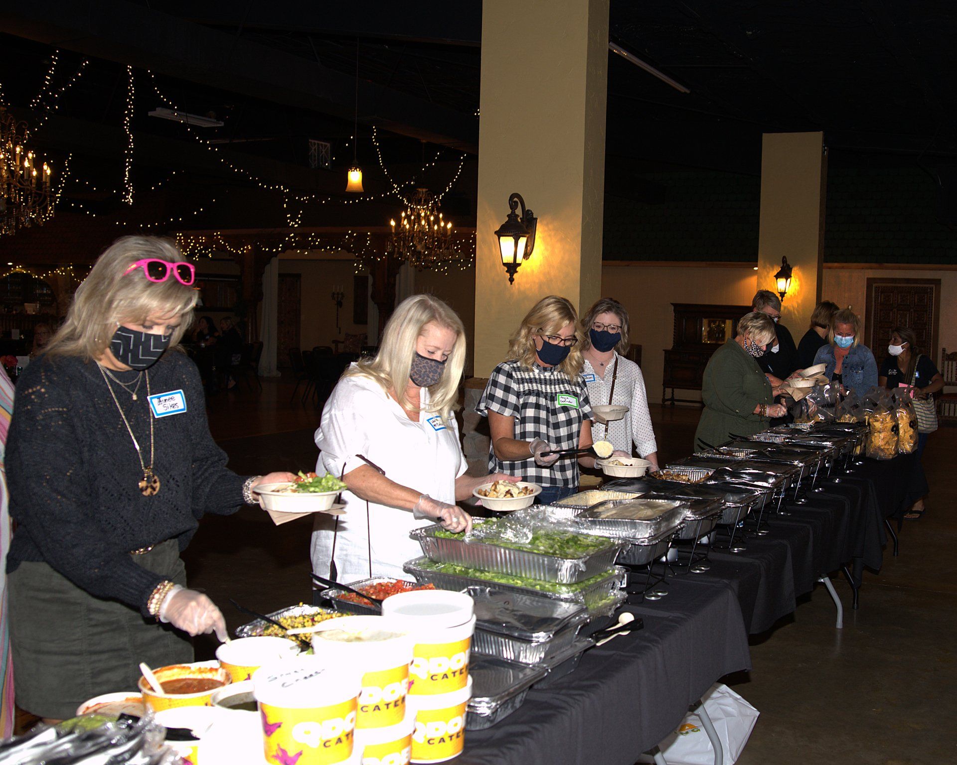 A group of people are standing around a long table eating food.