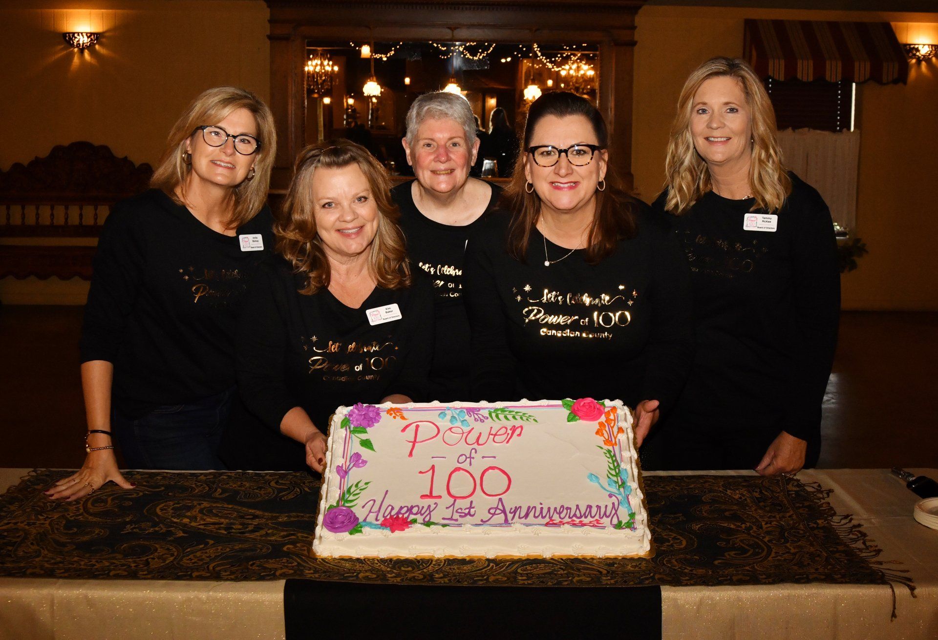 A group of women standing around a cake that says 100