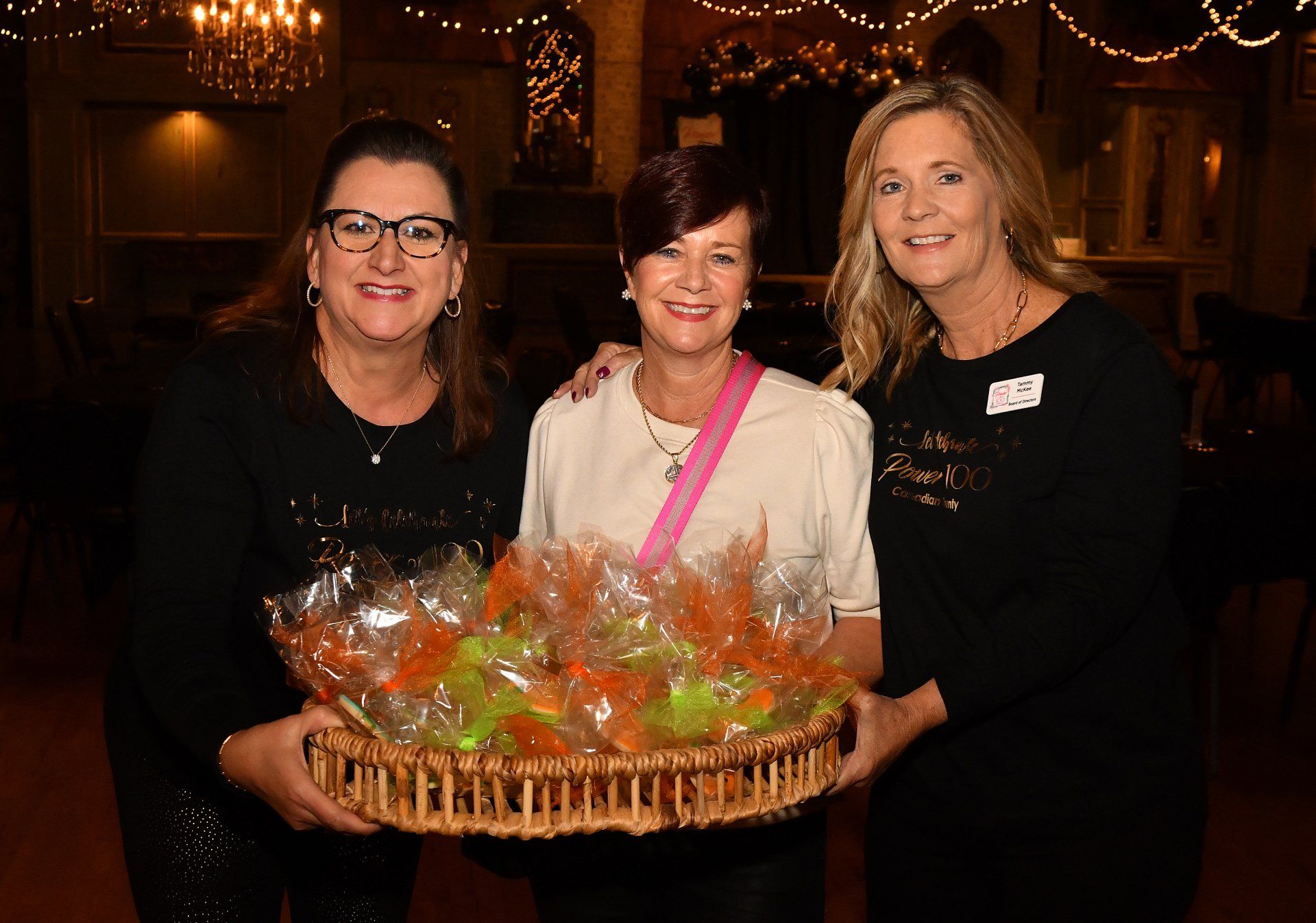 Three women are standing next to each other holding a basket of candy.
