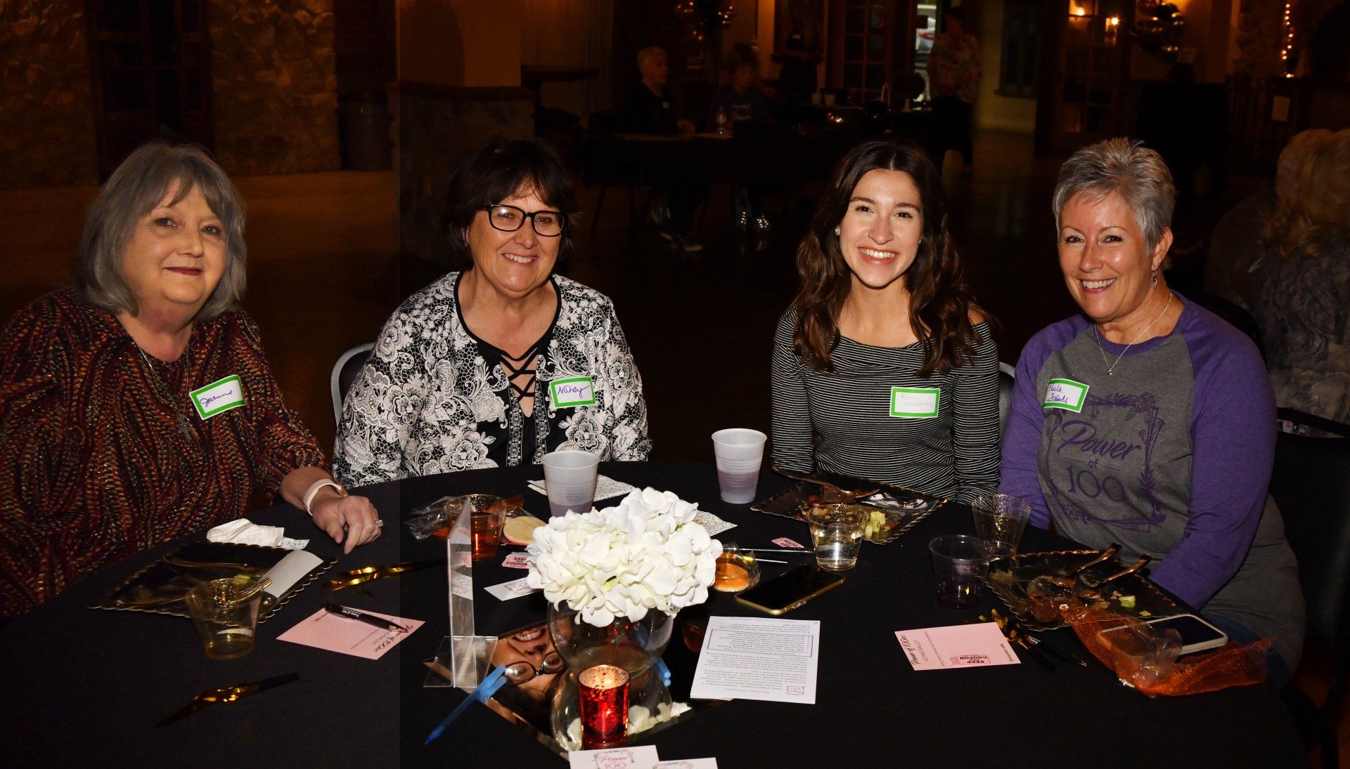 A group of women are sitting at a table with a vase of flowers.