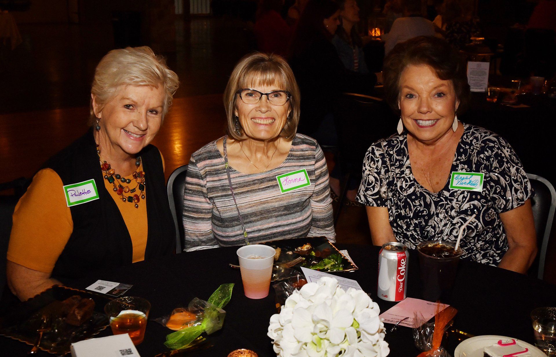 Three women are sitting at a table with drinks and food.