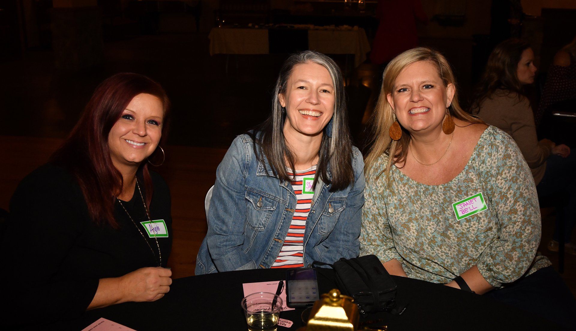 Three women are posing for a picture while sitting at a table.