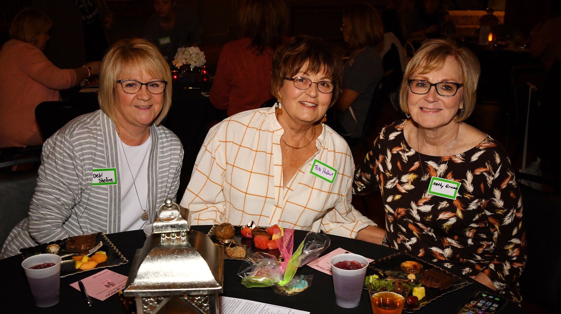 Three women are sitting at a table with drinks and food.