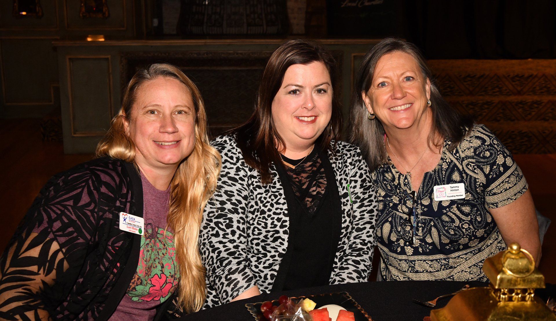 Three women are posing for a picture while sitting at a table.