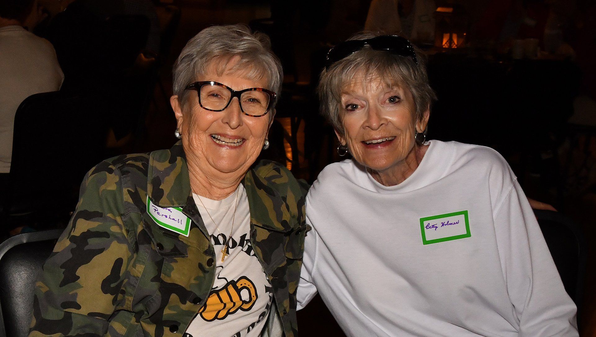 Two older women are posing for a picture together in a dark room.