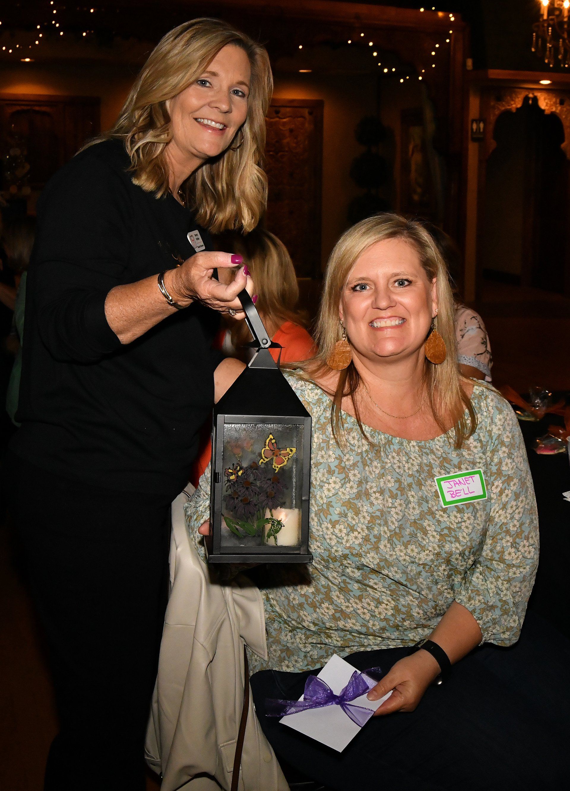 Two women are sitting at a table and one is holding a lantern.