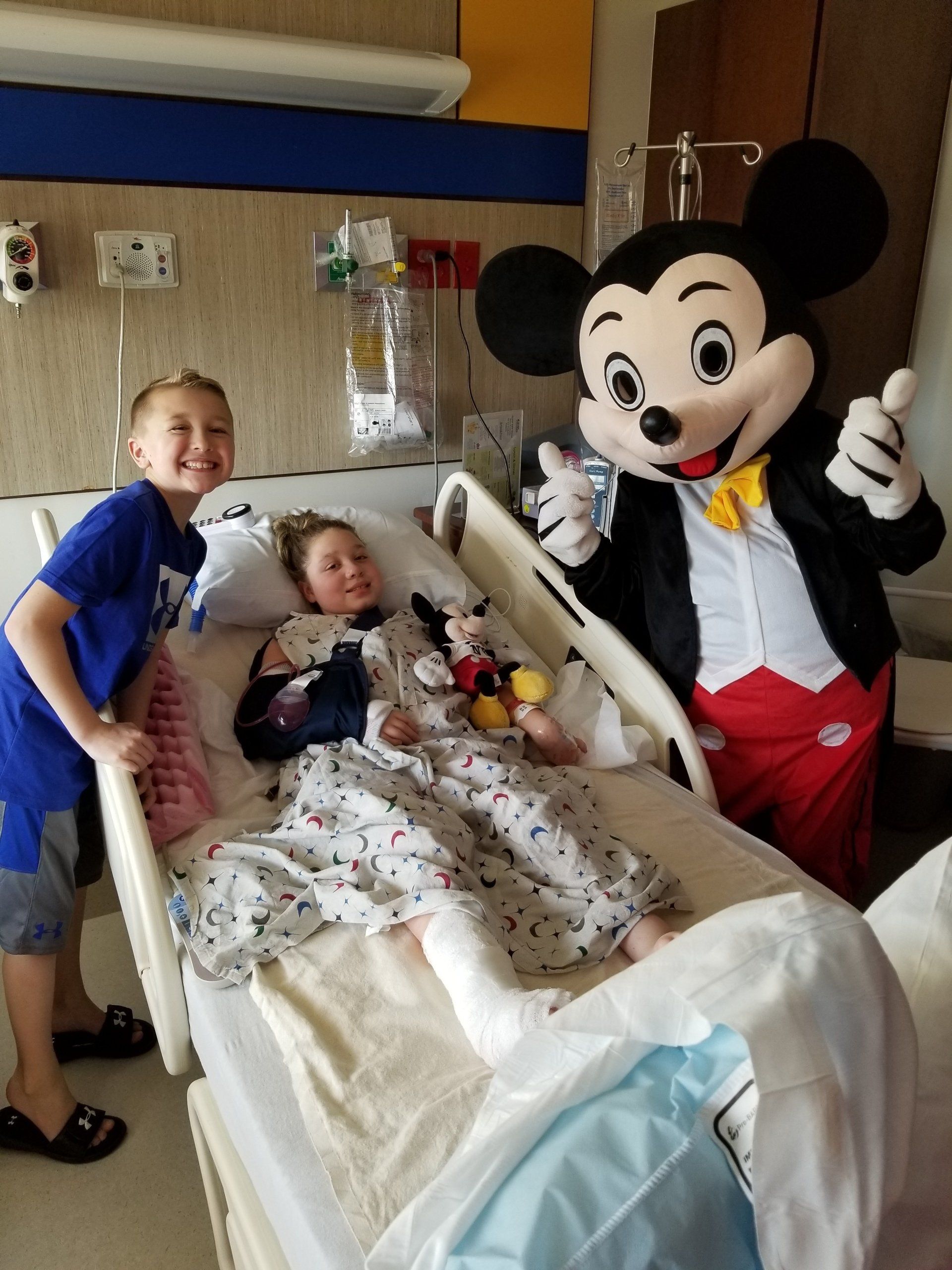 Mickey mouse is giving a thumbs up to a child in a hospital bed