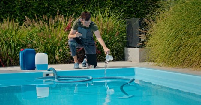 Man testing pool water with a reagent, kneeling near the edge of a blue pool. Blue containers are visible nearby.