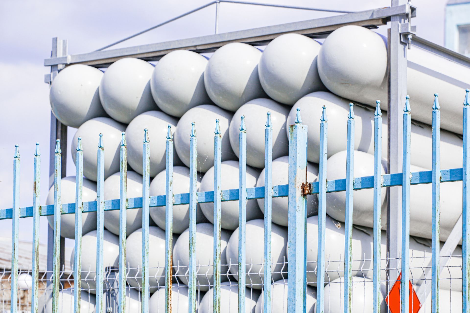 An image of rows of white propane gas cylinders stacked on top of each other behind a fence.