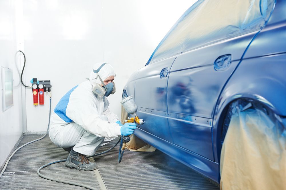 A Man Is Painting a Blue Car in A Paint Booth — Lyons Street Paint Panel in Bungalow, QLD
