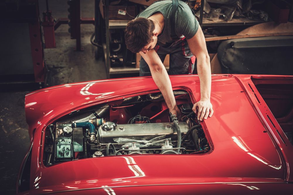 A Man Is Working On The Engine Of A Red Car In A Garage — Lyons Street Paint Panel in Bungalow, QLD