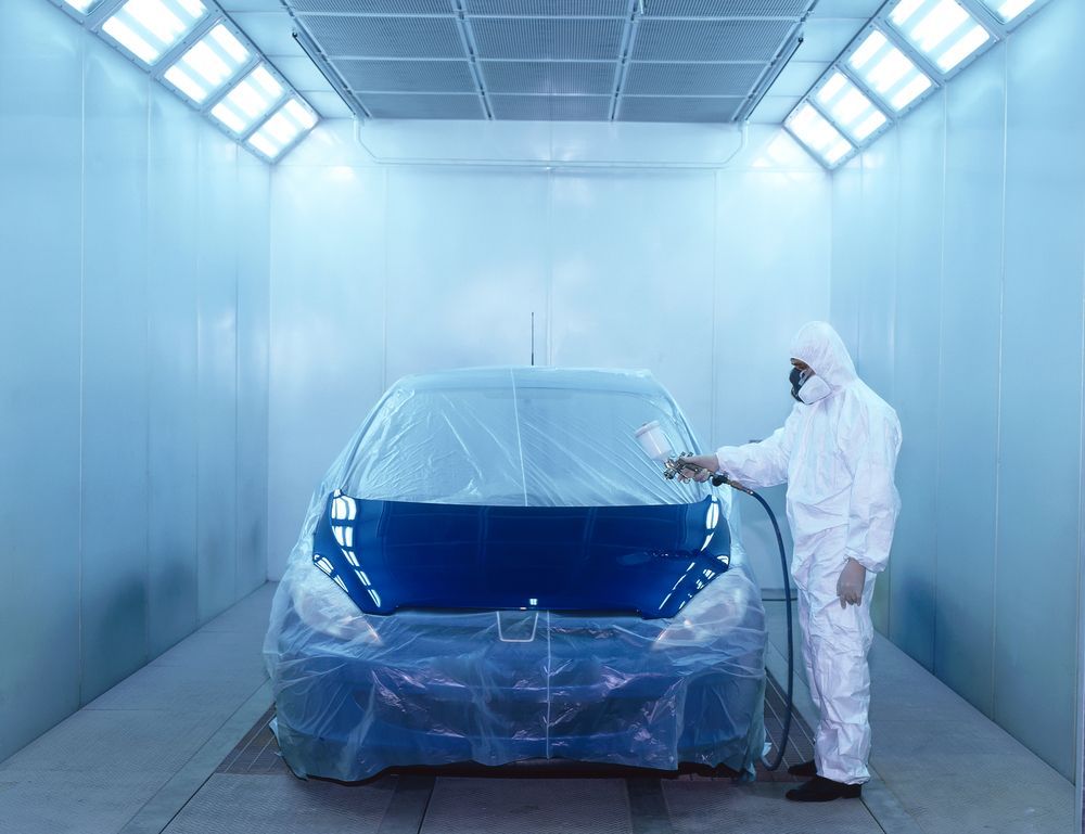 A Man Is Painting a Blue Car in A Paint Booth — Lyons Street Paint Panel in Bungalow, QLD