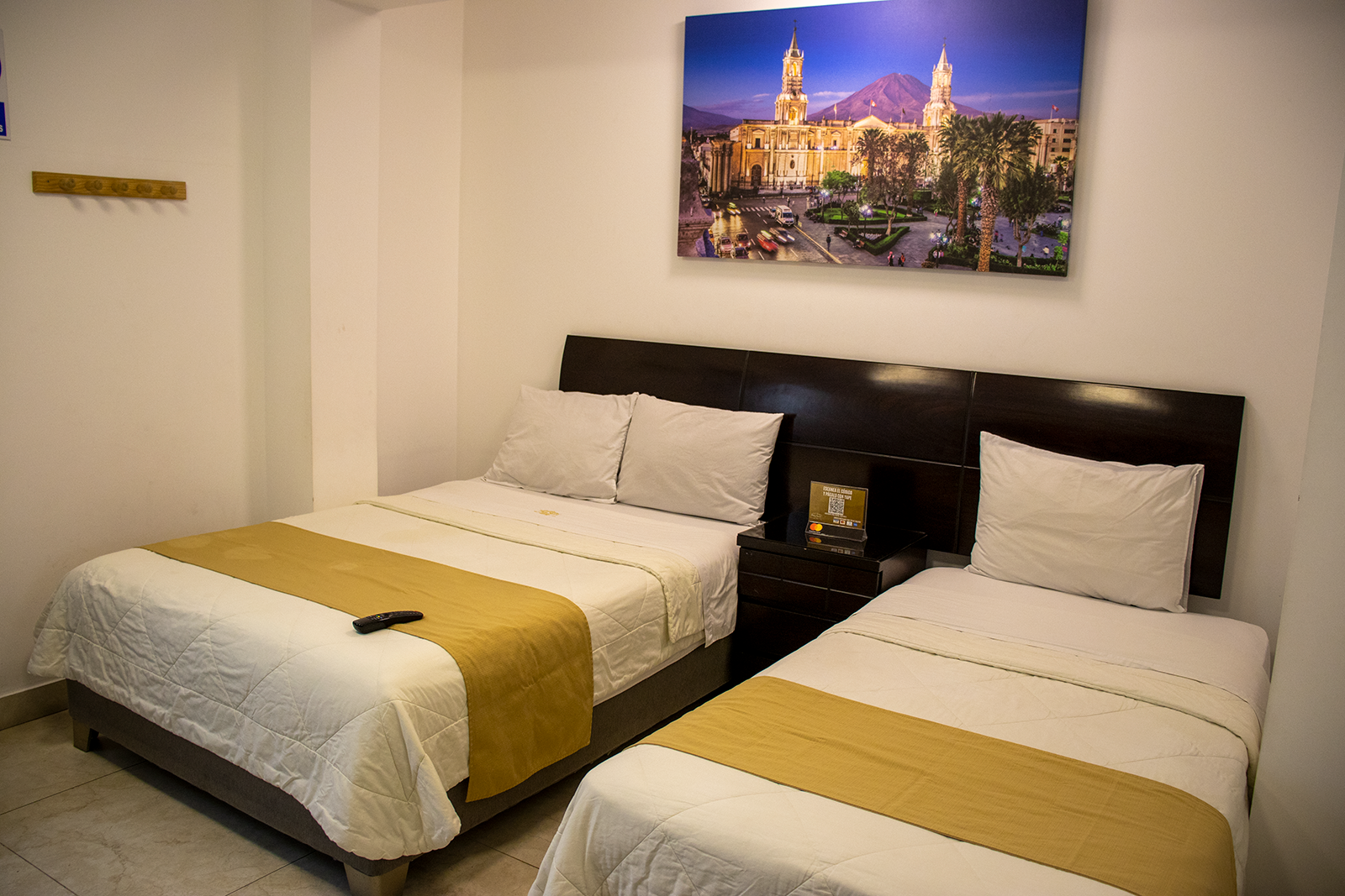 Habitación de hotel con dos camas, una doble y una individual, con un cuadro de paisaje en la pared.