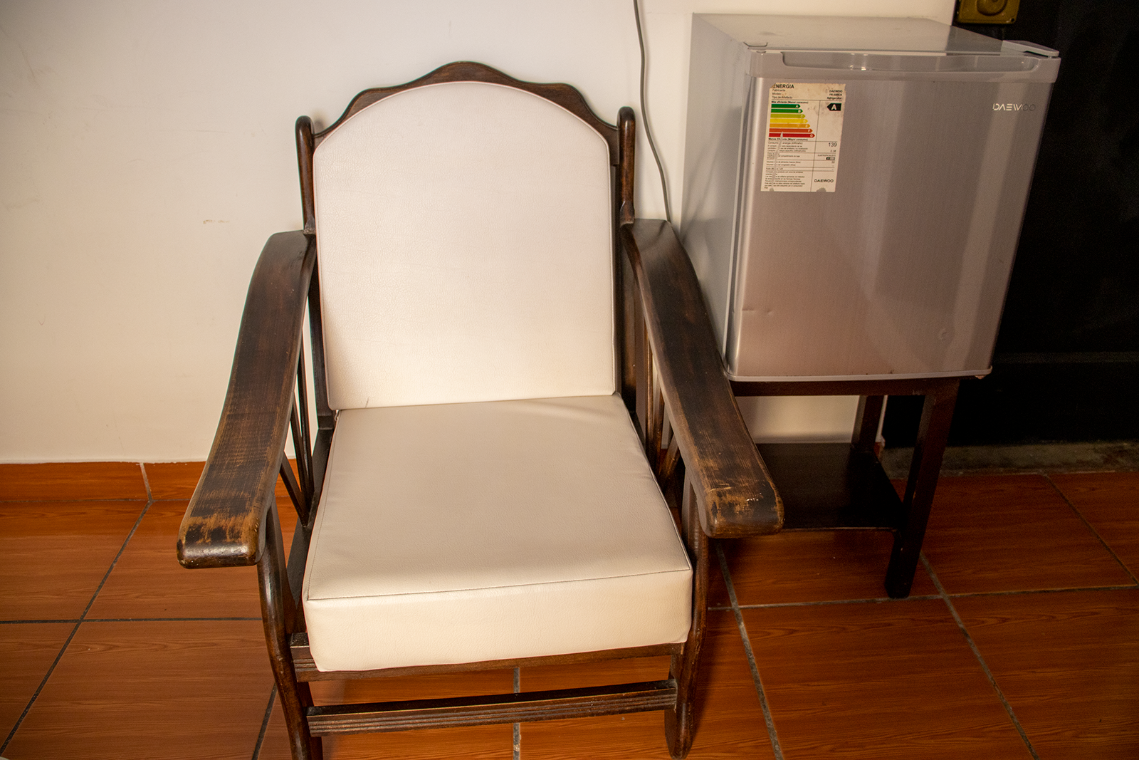 Mecedora de madera con cojín blanco junto a una mininevera sobre un pequeño soporte.