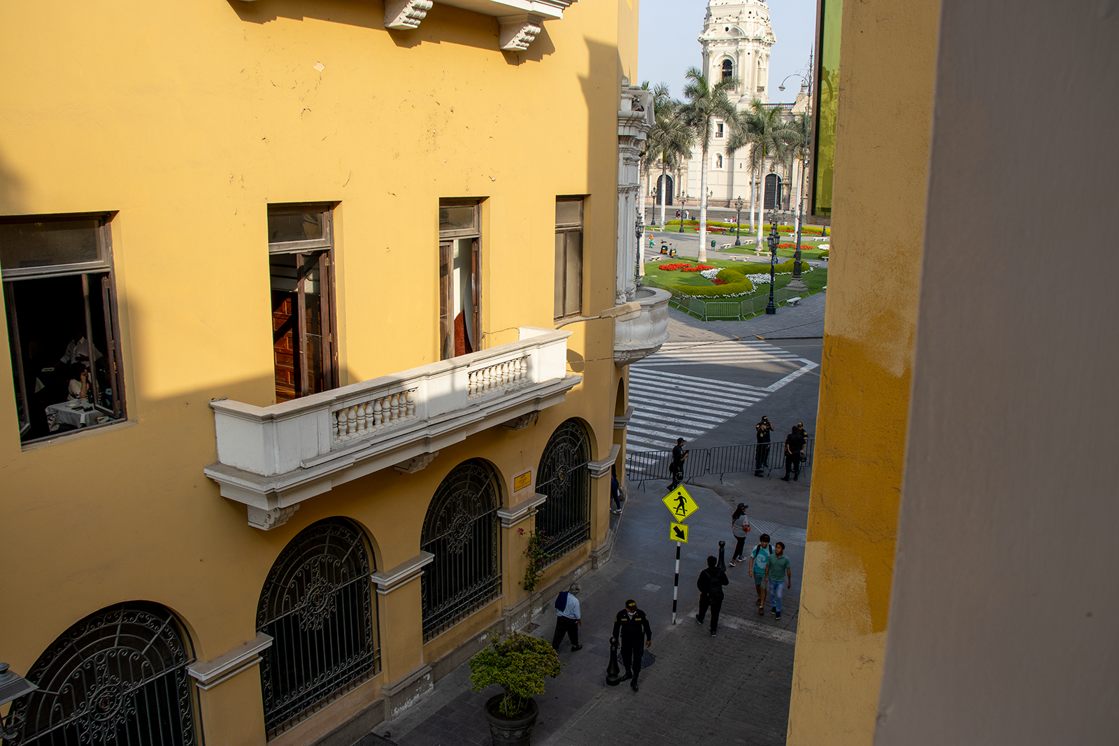 Edificio amarillo con balcón con vista a una plaza de la ciudad con gente y una iglesia.
