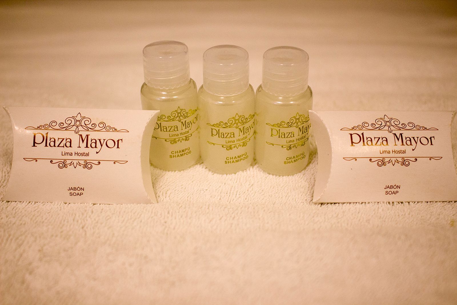 Tres pequeñas botellas de champú y dos jabones sobre una toalla blanca, con una etiqueta que dice 