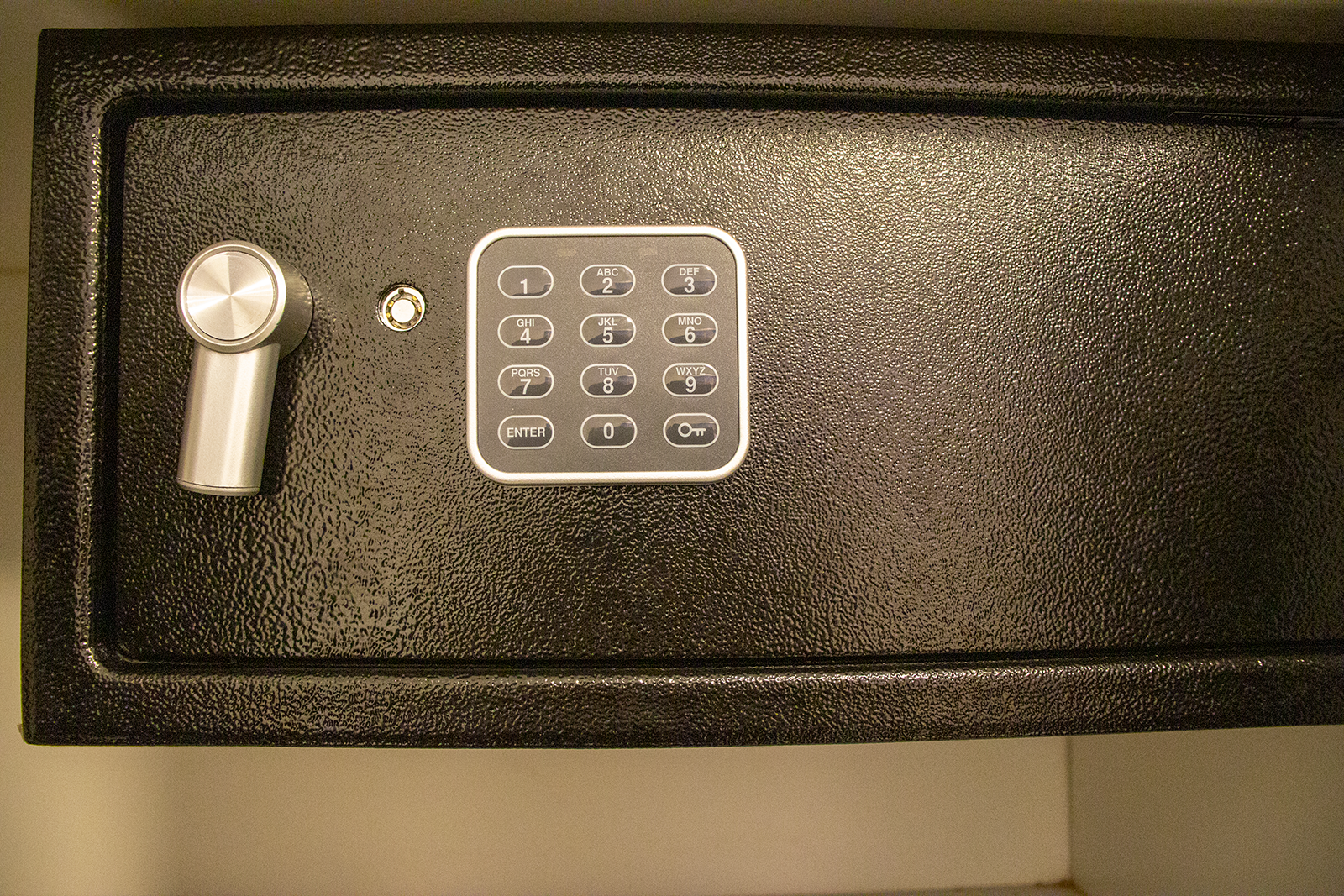 Primer plano de una caja fuerte negra con teclado y cerradura con llave en su puerta.