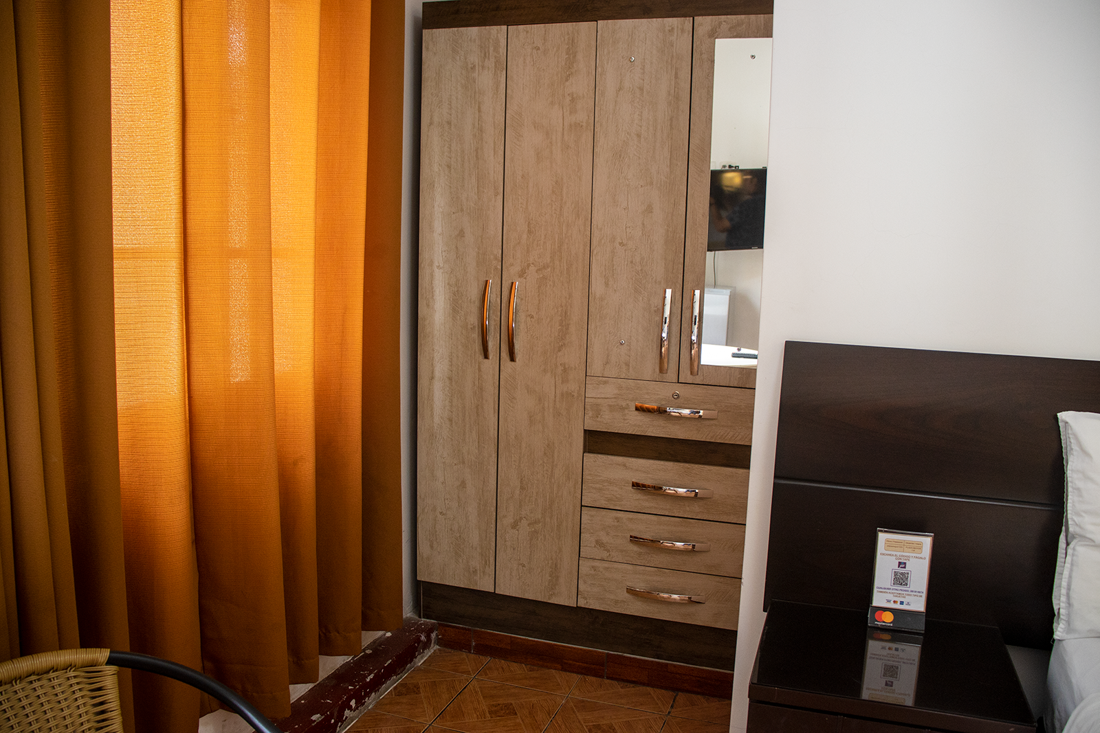 Rincón de dormitorio con armario, cortinas naranjas y mesita de noche.