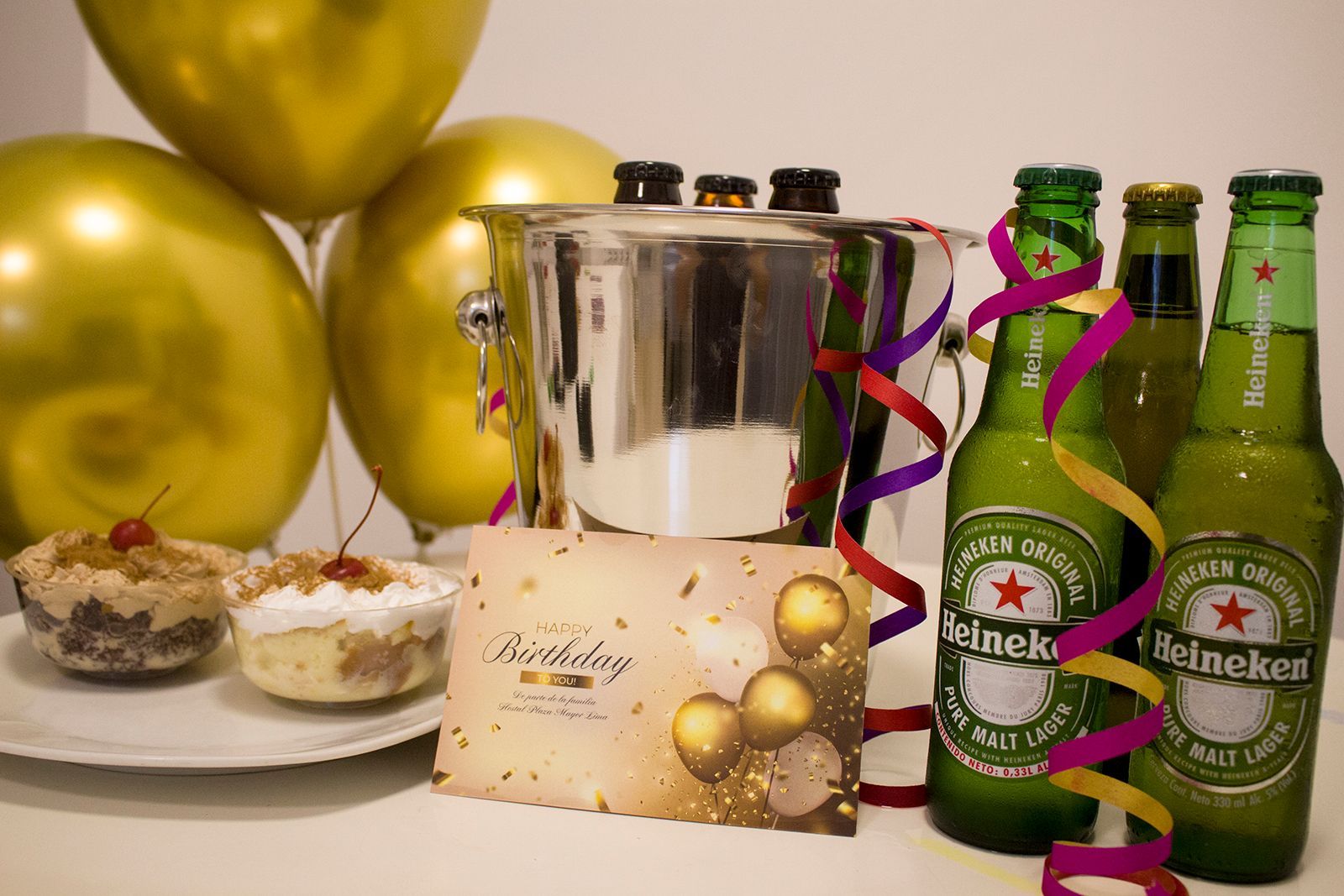 Celebración de cumpleaños con cerveza, pastel, globos y una tarjeta.
