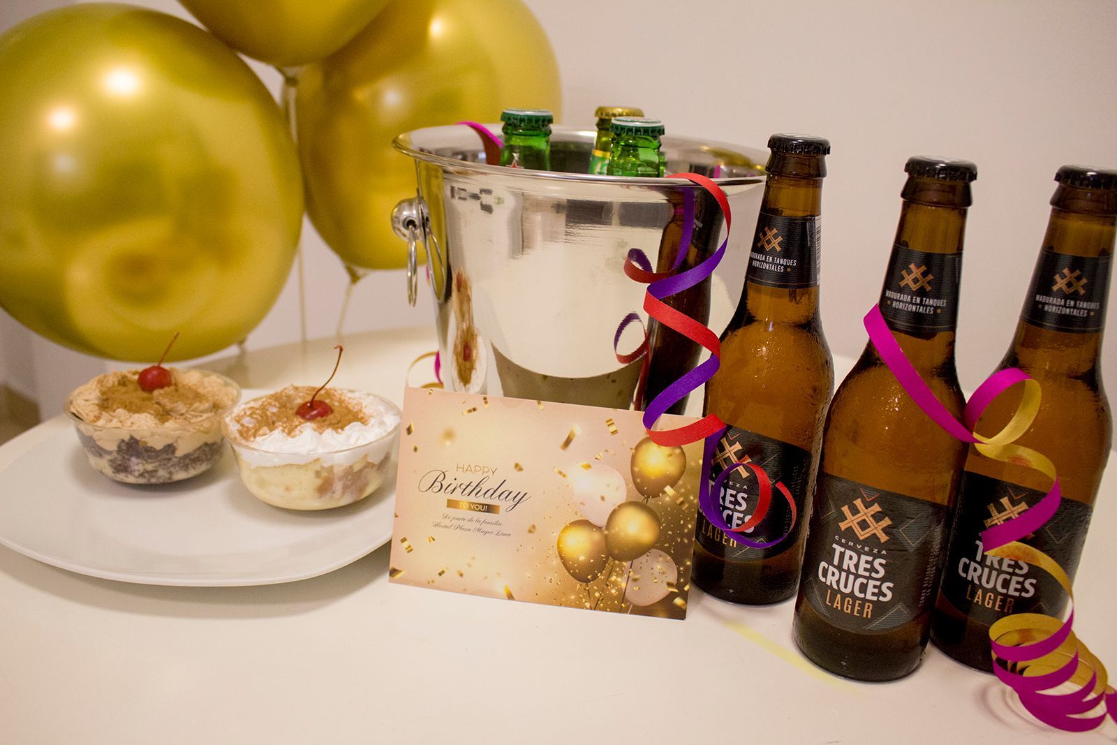 Decoración de cumpleaños con botellas de cerveza, hielera, globos, cupcakes y una tarjeta.