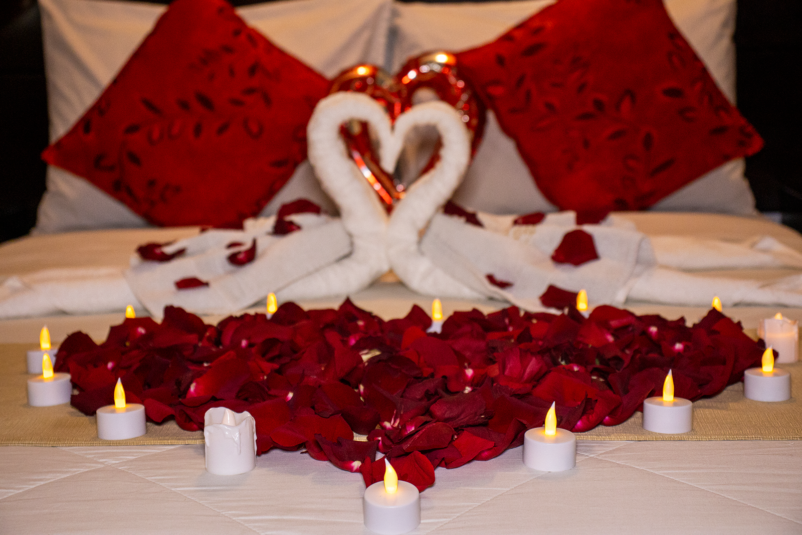 Cama romántica decorada con pétalos de rosas rojas, velas y cisnes de toalla, para una ocasión especial.