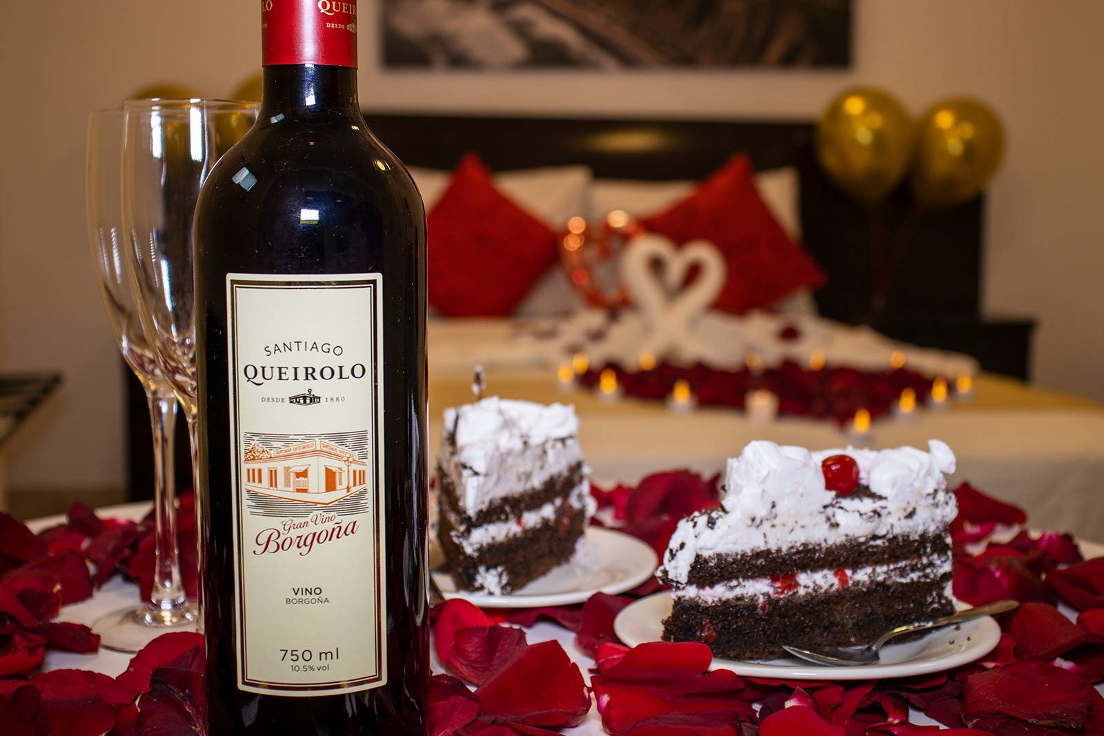 Configuración romántica con vino tinto, pastel, rosas y cama decorada.