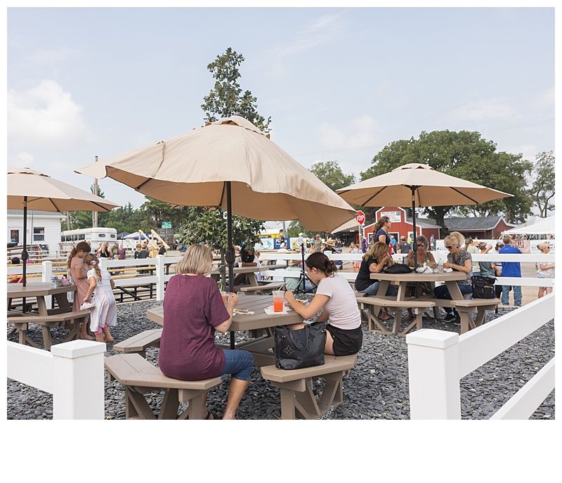 Outdoor seating area with people at picnic tables under umbrellas.