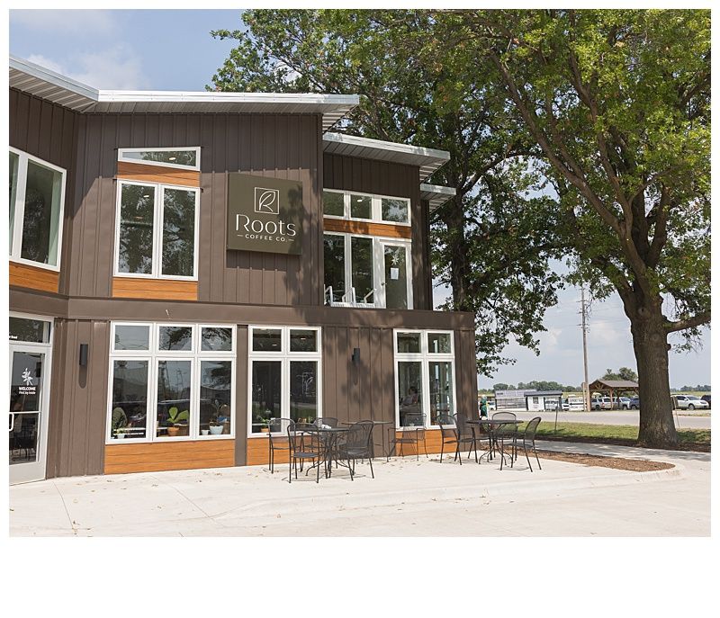 Brown two-story building with white-framed windows, outdoor seating, and a sign that reads