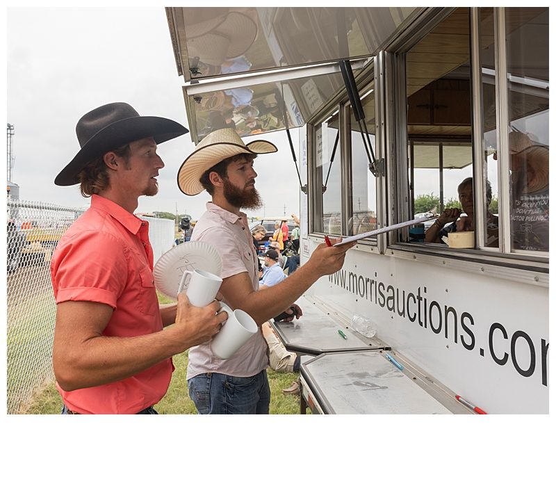 Two men in cowboy hats at a food truck, one handing a cup to the window.