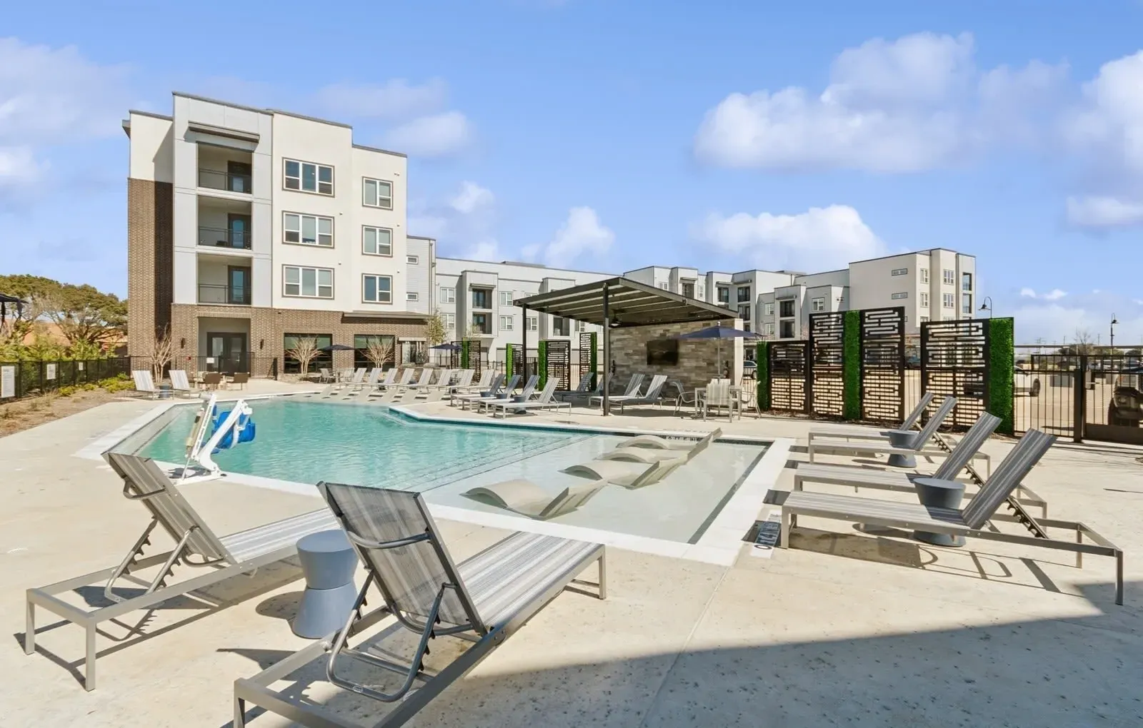 Outdoor community pool at apartment complex with lounge chairs and shade canopy. Explore these beautifully designed apartments in Rowlett, TX and envision your next home—schedule a tour today.