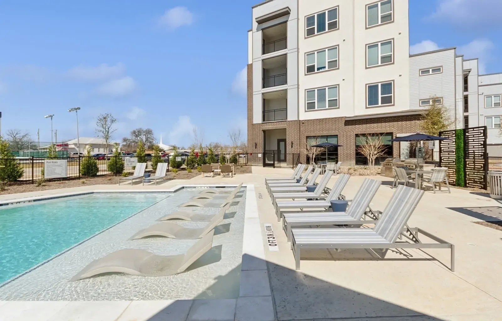 Outdoor apartment pool with lounge chairs and a modern building in the background. Discover modern living at Rowlett TX apartments and picture your day-to-day—learn more online.