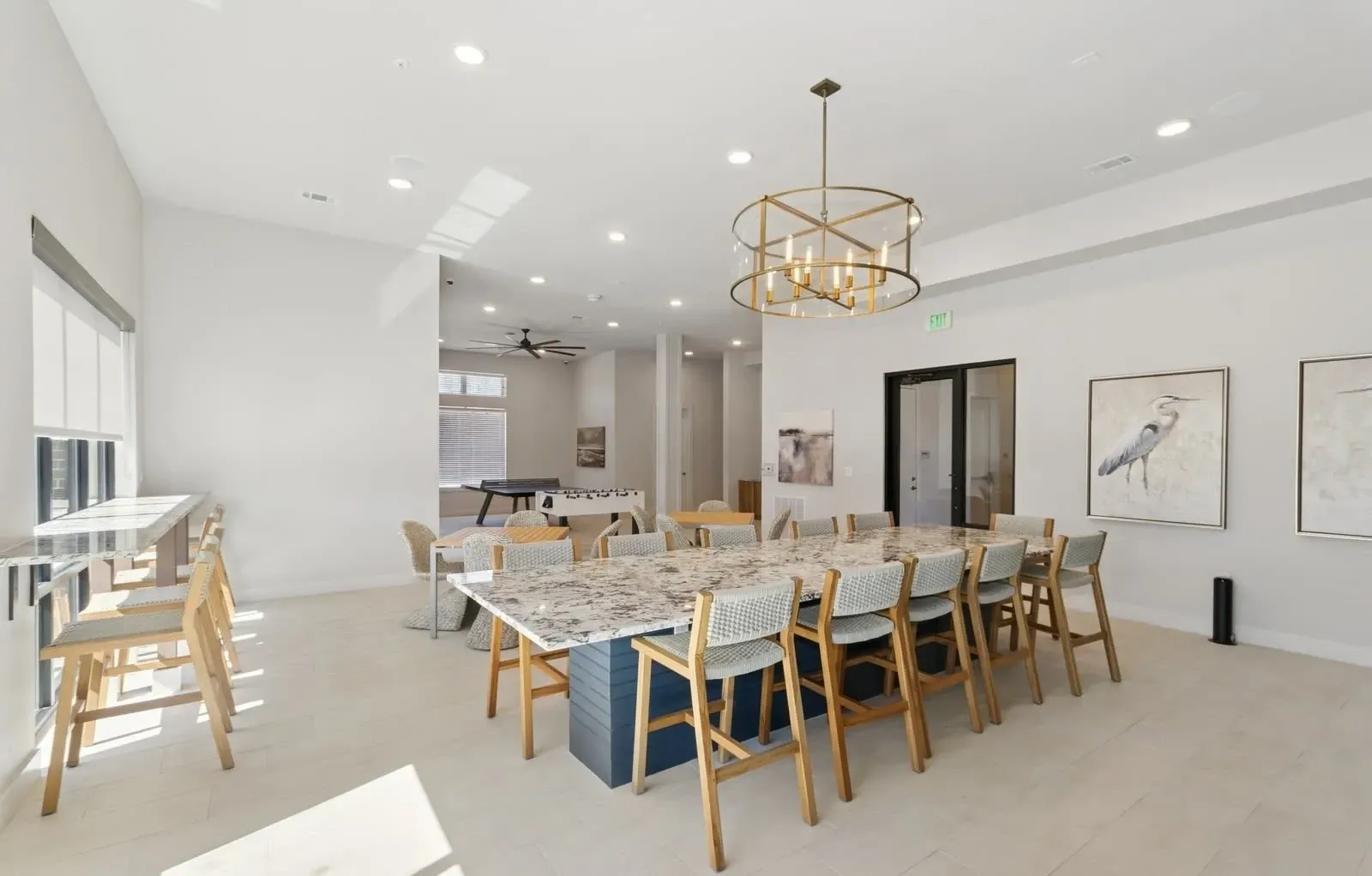 Bright community lounge with a large marble-top table, chairs, and wall art. Enjoy elevated living at luxury apartment homes near Pecan Grove Park—explore availability now.