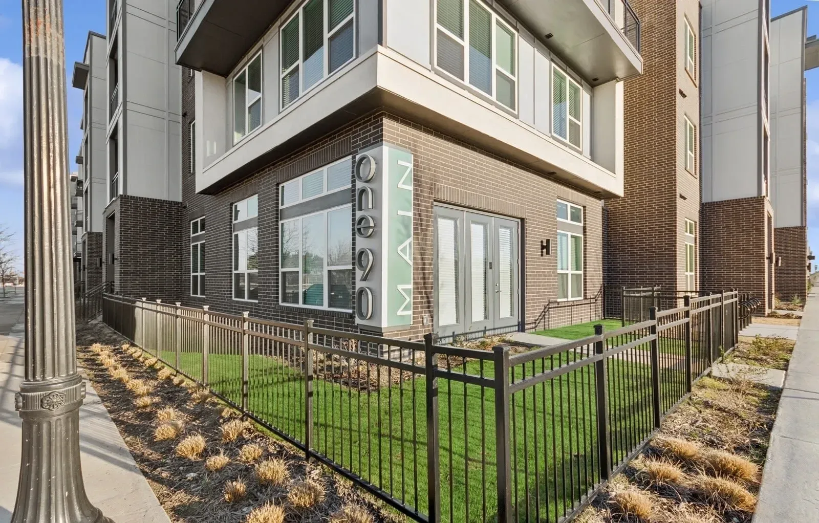 Exterior view of a modern apartment building with brick lower level, large windows, and a black metal fence. Discover convenience at pet-friendly apartments in Rowlett, TX with a dog park—bring your companion and visit.
