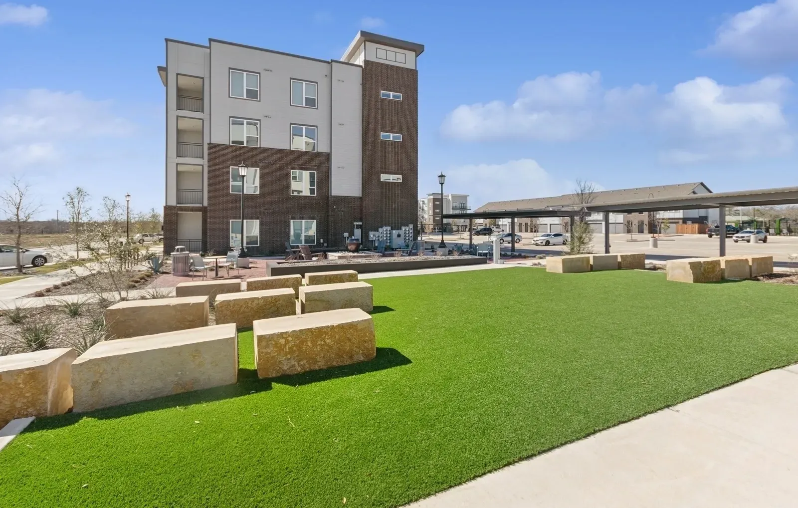 Exterior view of a modern apartment building with a green lawn and stone seating. Stay close to care at apartments near Baylor Scott & White Rowlett, TX—see available homes today.