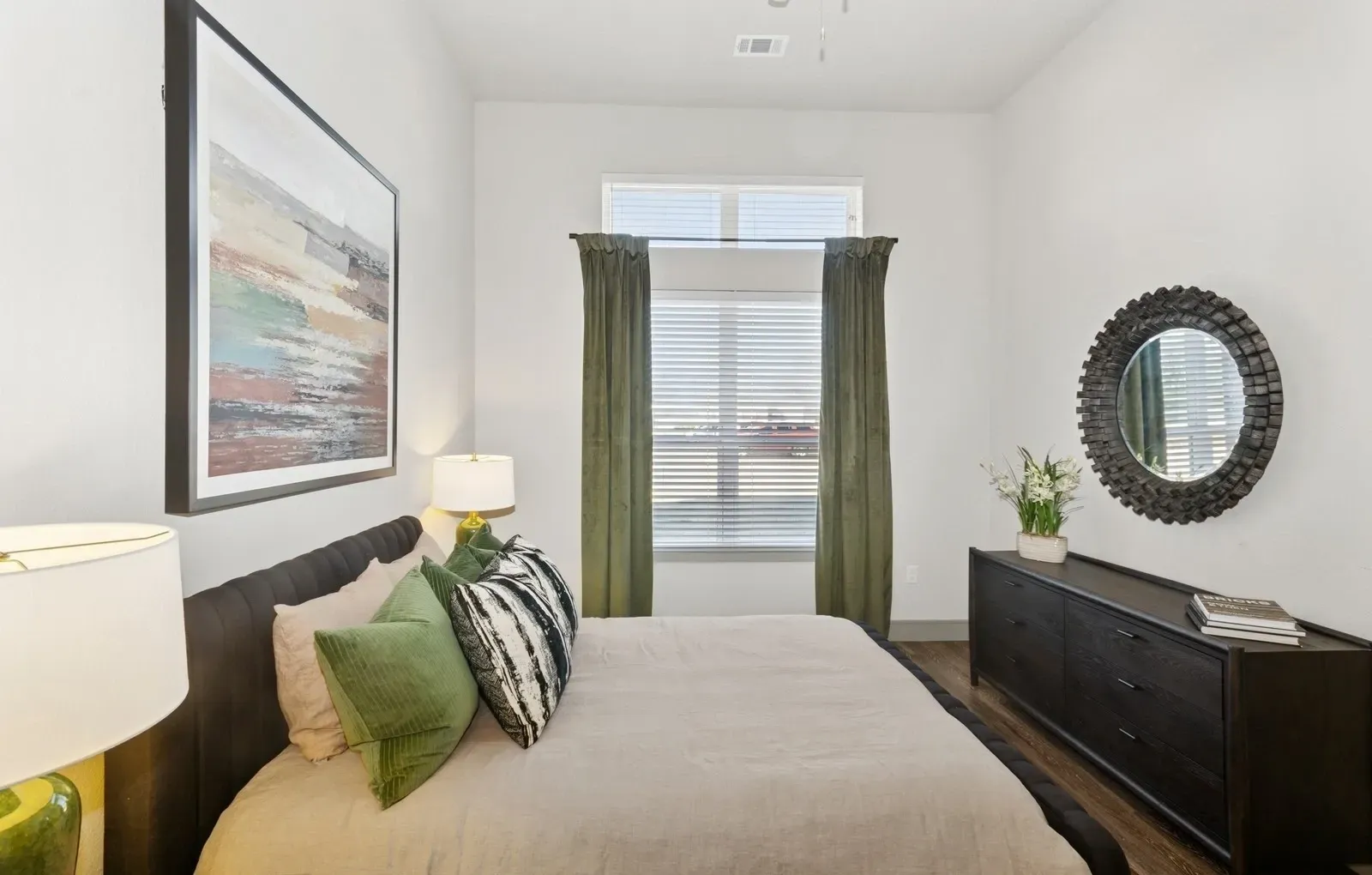 Bedroom in a modern apartment with a bed, dresser, and round mirror. Prioritize wellness at apartments with fitness center Rowlett, TX—take a closer look and book a tour.