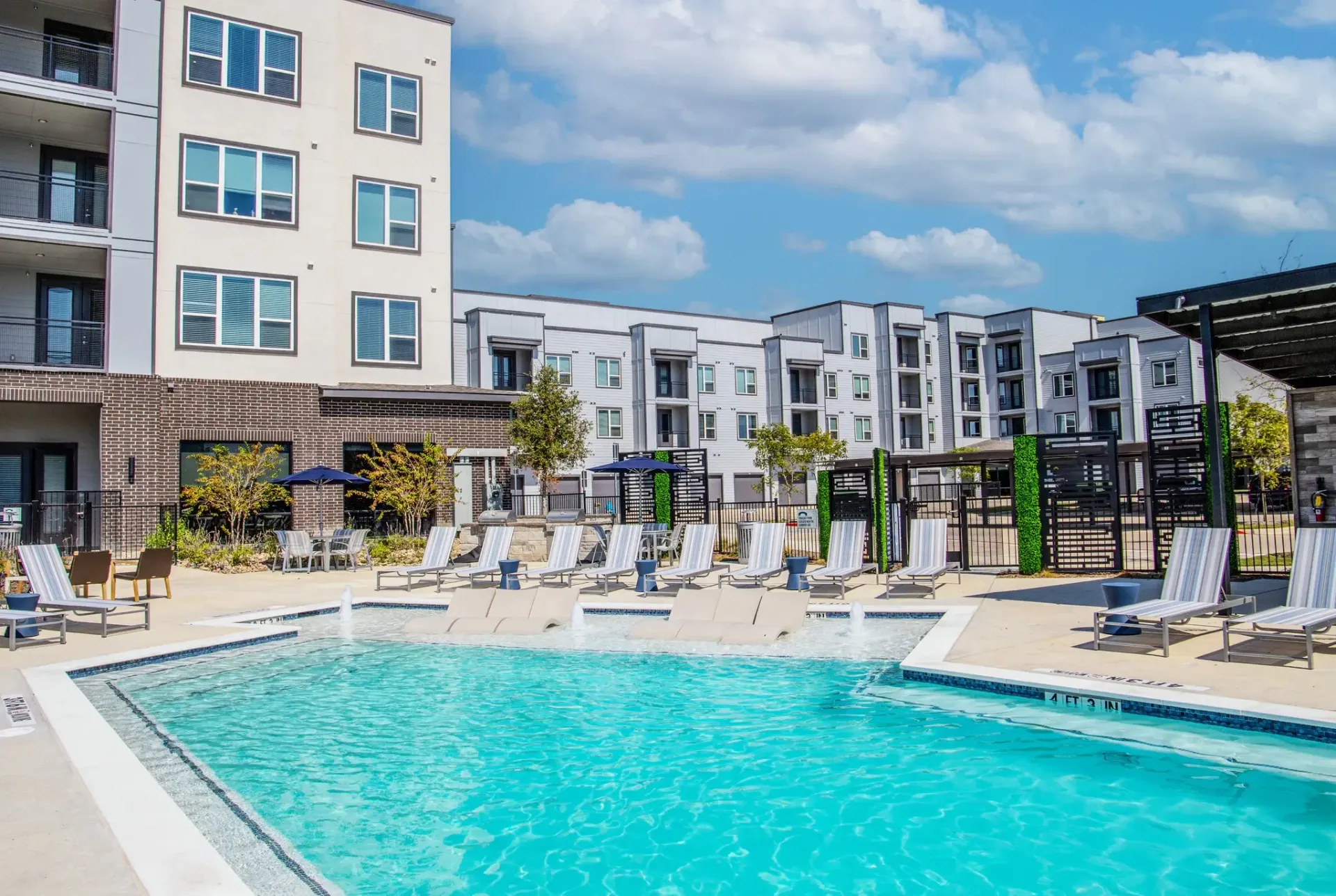 Outdoor communal pool area with turquoise water, white lounge chairs, and surrounding modern apartment buildings. Enjoy connectivity at apartments near downtown Rowlett DART Blue Line—find your next home today.