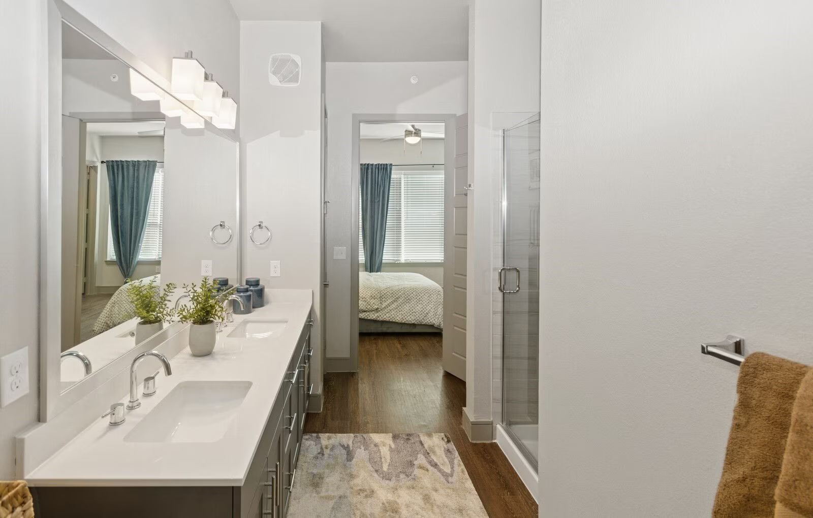 Modern white bathroom with double sinks, mirrors, and a doorway to a bedroom with a bed and teal curtains