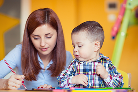 A woman is teaching a child how to draw with pencils.