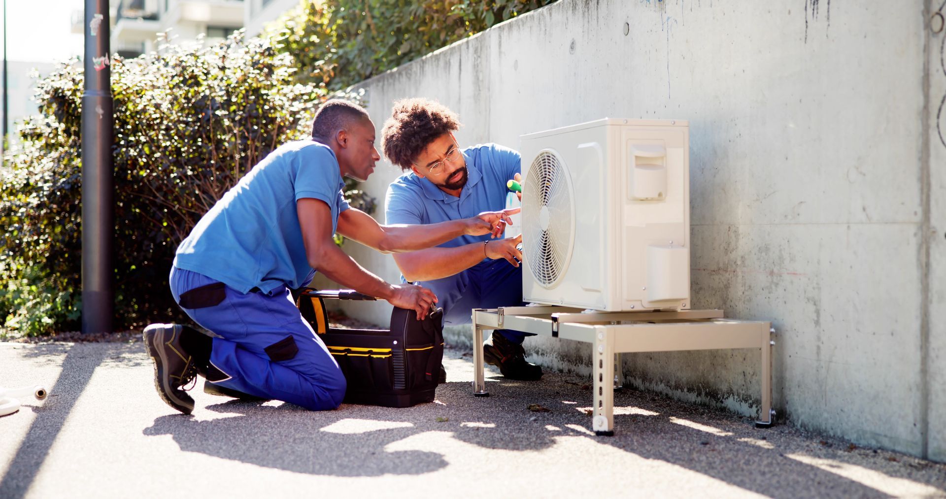 Two men are working on an air conditioner outside.