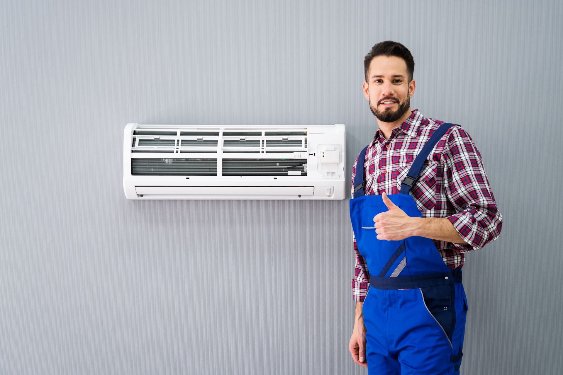 A man is standing in front of an air conditioner and giving a thumbs up.