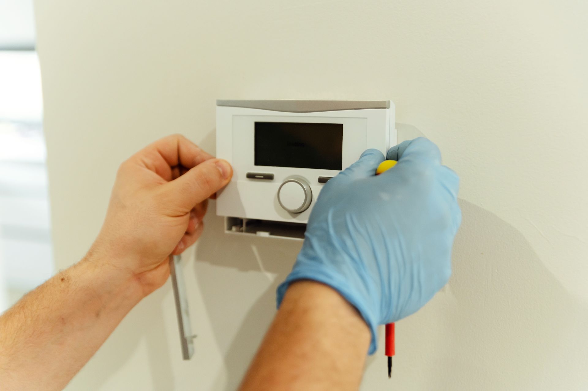 A person wearing blue gloves is installing a thermostat on a wall.