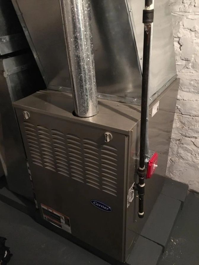A furnace is sitting in a basement next to a pipe.