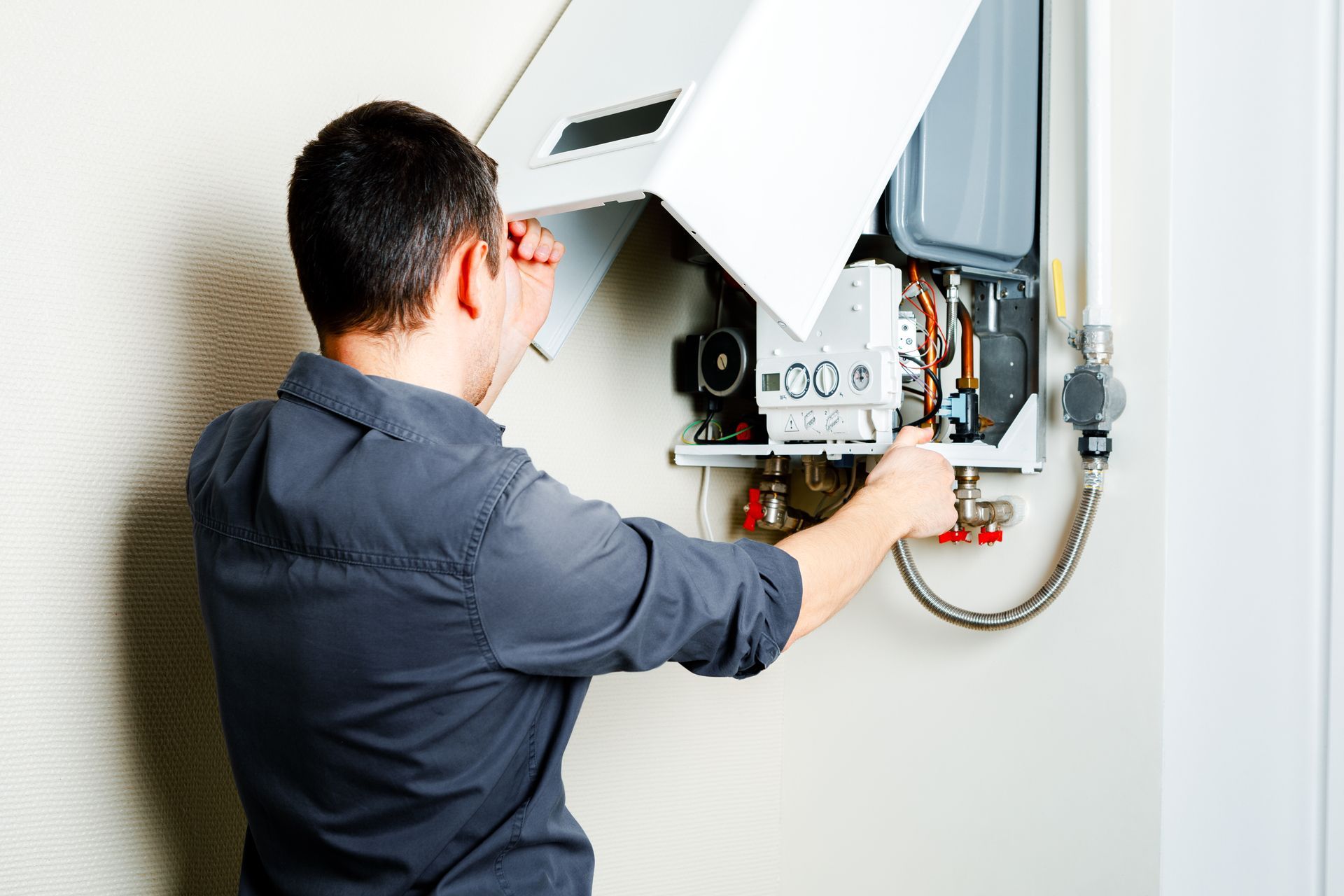 A man is kneeling down in front of a boiler and looking at a tablet.